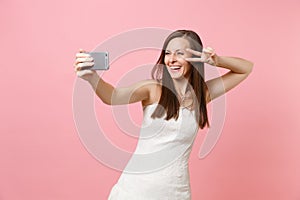 Portrait of joyful bride woman in elegant white wedding dress showing victory sign doing taking selfie shot on mobile