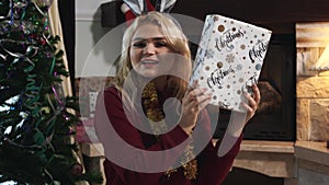 Portrait of joyful caucasian blond woman catching Christmas present and shaking the box. smiling young girl sitting next
