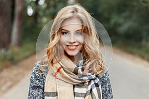 Portrait of a joyful cute young woman with a smile with blue eyes in an elegant coat with a checkered stylish scarf