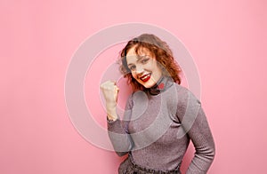 Portrait of joyful girl with bright makeup rejoices to win against pink background, looks into camera and smiles. Happy lady with