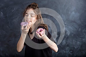 Portrait of joyful girl with donuts on black background. Happy girl holds fresh donuts and looks at them. Good mood, diet concept