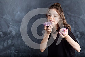 Portrait of joyful girl with donuts on black background. Happy girl holds fresh donuts and looks at them. Good mood, diet concept