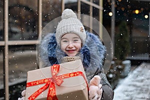 Portrait of joyful girl with a gift box for Christmas on a city street in winter with snow on a festive market with decorations