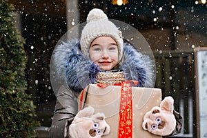 Portrait of joyful girl with a gift box for Christmas on a city street in winter with snow on a festive market with decorations