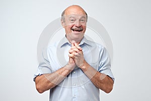 Portrait of joyful handsome mature man clapd palms, waits to hear something pleasant, recieves compliments