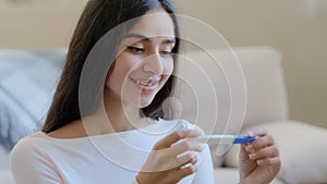 Portrait of joyful happy pregnant woman future mom sits at home holds pregnancy positive test result. Beautiful arabian