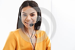 Portrait of joyful hotline assistant woman wearing microphone headset speaking with customer by phone in office