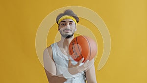 Portrait of joyful Indian guy having fun with basketball playing alone on yellow background