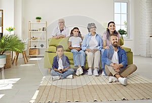 Portrait of joyful large family of three generations enjoying watching funny TV talk show together.