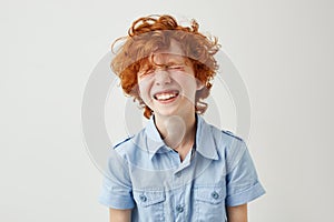 Portrait of joyful little boy with ginger hair and freckles laughing out loud with closed eyes in classroom during break