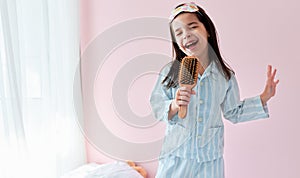 Portrait of a joyful little girl in pajama on the bed holding a hair brush like microphone singing imitates herself a real singer