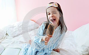 Portrait of a joyful little girl in pajama holding a hair brush like microphone singing imitates herself a real singer in the