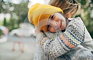 Portrait of a joyful little girl in a yellow hat smiling and hugging her mom in the park. Mother`s day.
