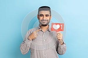 Portrait of joyful man pointing at heart like icon, recommending to click on social media button.