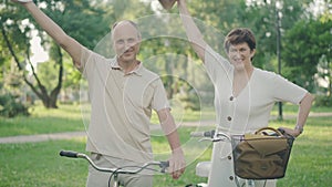 Portrait of joyful man and woman taking off hats and smiling at camera. Positive Caucasian couple posing in summer park