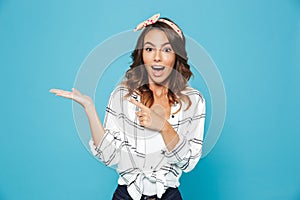 Portrait of joyful pretty girl 20s wearing casual clothing smiling and holding copyspace at palm, isolated over blue background