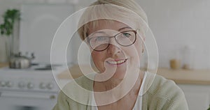 Portrait of joyful retired woman in eyeglasses smiling expressing happiness looking at camera in kitchen