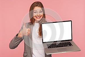 Portrait of joyful satisfied brunette businesswoman in elegant suit showing thumbs up and holding laptop