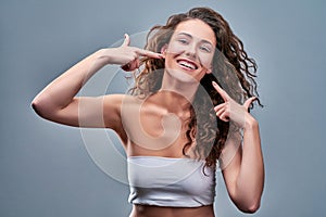 Portrait of joyful satisfied girl gesturing her beaming white healthy teeth with two forefingers looking at camera  on photo