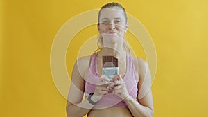 Portrait of joyful sports lady smelling chololate then eating and smiling on yellow background