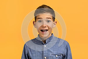 Portrait of joyful surprised teenage boy posing against yellow studio background