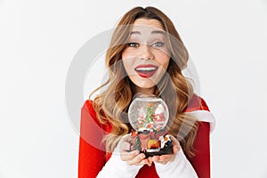 Portrait of joyful woman 20s wearing Santa Claus red costume smiling and holding Christmas snow ball, isolated over white