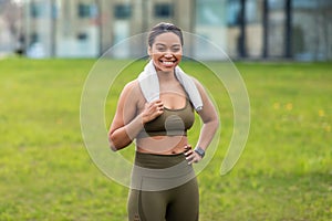 Portrait of joyful young black woman in sportswear with towel posing at park, copy space