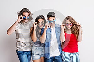 Portrait of joyful young group of friends with funky sunglasses standing in a studio.