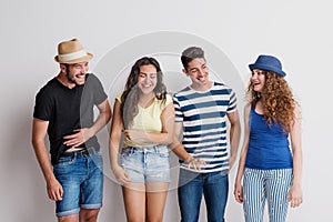 Portrait of joyful young group of friends with hats standing in a studio, laughing.