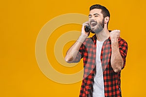 Portrait of a joyful young man holding mobile phone isolated over yellow background, celebrating