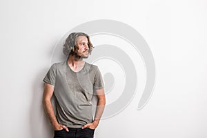 Portrait of a joyful young man with long wavy hair in a studio, hands in pockets.