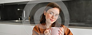 Portrait of a joyful young woman enjoying a cup of coffee at home. Smiling beautiful girl drinks hot tea in winter