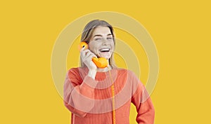 Portrait of joyful young woman talking on landline phone isolated on yellow background.