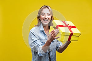 Portrait of joyous beautiful woman in denim shirt standing with opened gift box. studio shot  on yellow background