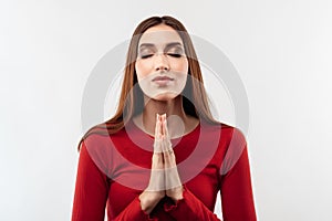 Portrait of joyous brunette woman with long hair in casual red sweater keeping palms together and praying