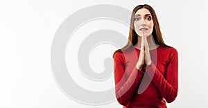 Portrait of joyous brunette woman with long hair in casual red sweater keeping palms together and praying. Copy space