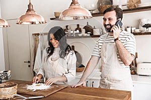 Portrait of joyous couple using smartphone while cooking together in kitchen at home