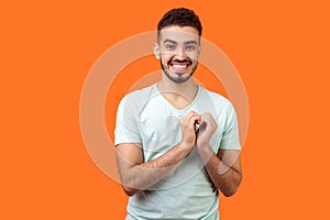 Portrait of joyous handsome brunette man in love making heart gesture. indoor studio shot isolated on orange background