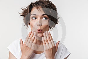 Portrait of joyous woman with short brown hair in basic t-shirt covering her mouth with hands