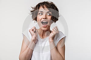 Portrait of joyous woman with short brown hair in basic t-shirt rejoicing and clenching fists