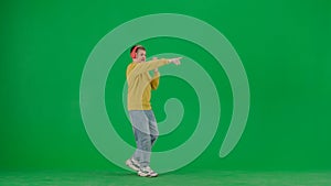 Portrait of kid boy on chroma key green screen. Schoolboy in jeans in headphones taking selfie video blog on smartphone