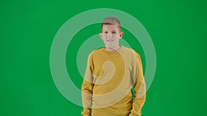 Portrait of kid boy on chroma key green screen. Schoolboy in jeans standing looking at the camera positive face