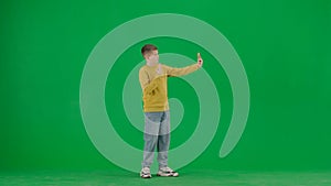 Portrait of kid boy on chroma key green screen. Schoolboy in jeans standing taking selfie video blog or photo on