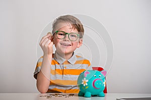 Portrait of kid boy putting money in the moneybox. Child save money while put coin in the piggy bank