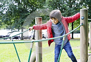 Portrait kid climbing rope in the playground. Child enjoying activity in a climbing adventure in the park. Cute little boy playing
