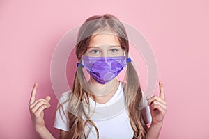 Portrait of kid with face mask pointing finger up on color background