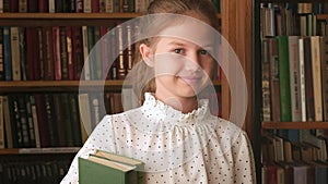 Portrait of kid girl with books in old library close up. Schoolgirl selecting literature for reading