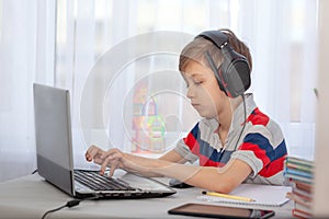 Portrait kid in headphones typing on computer, studying in home. Education distance learning