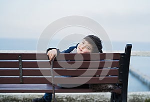 Portrait  kid looking at camera with smiling face, Healhty ,Happy child sitting on bench with blurry sea background. Yong boy