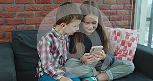 Portrait of kids looking at mobile phone at home. Sister and brother playing video games on mobile phone.